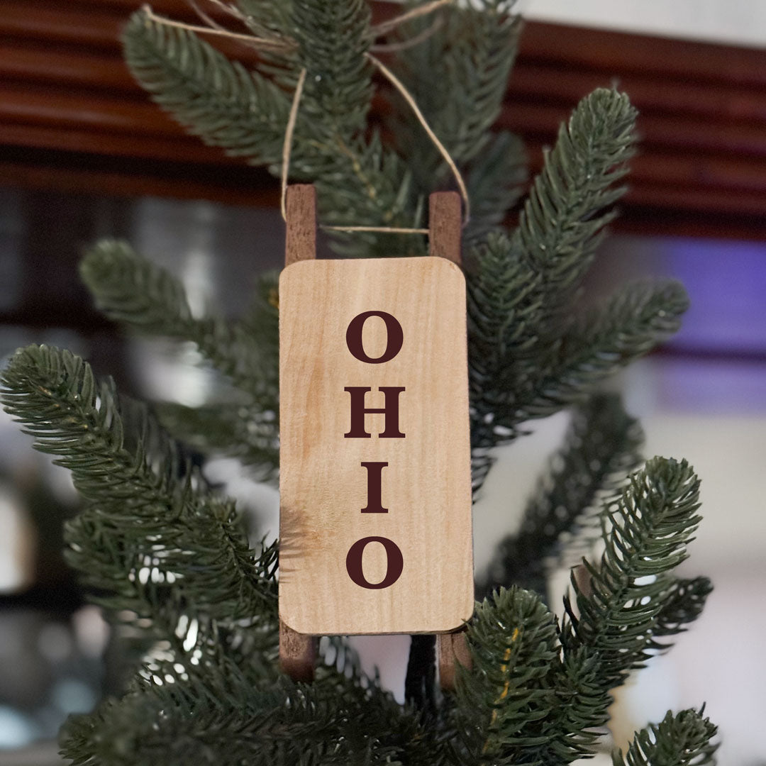 Handmade wood sled ornament with the word OHIO laser engraved design. Hung on a green artificial pine tree. 